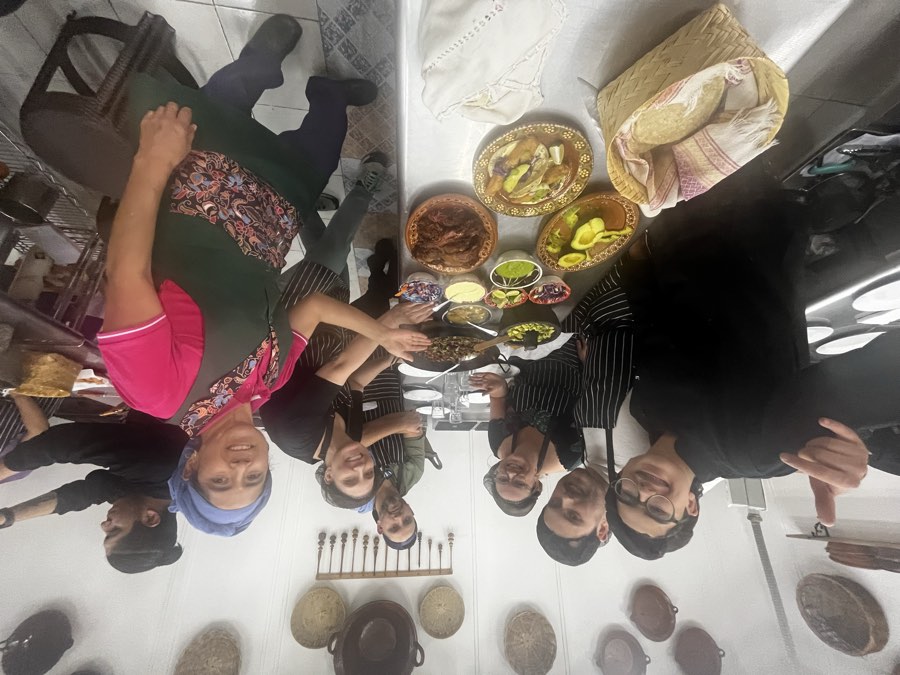 A cooking class group in aprons gathered around a table of finished dishes